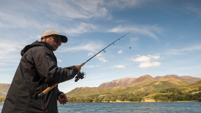 Man with baseball cap and sunglasses holding a rod fishing on Buttermere